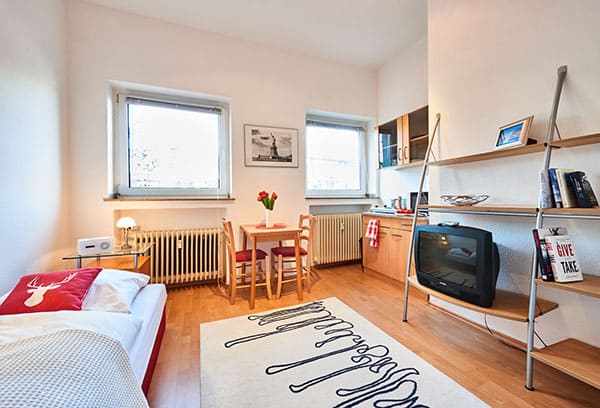 1-Raum-Appartement App524 Wohnbereich: Bett Nachttisch Essbereich Küche Theke Kochplatte Mikrowelle Regal TV Laminat 600px breit
